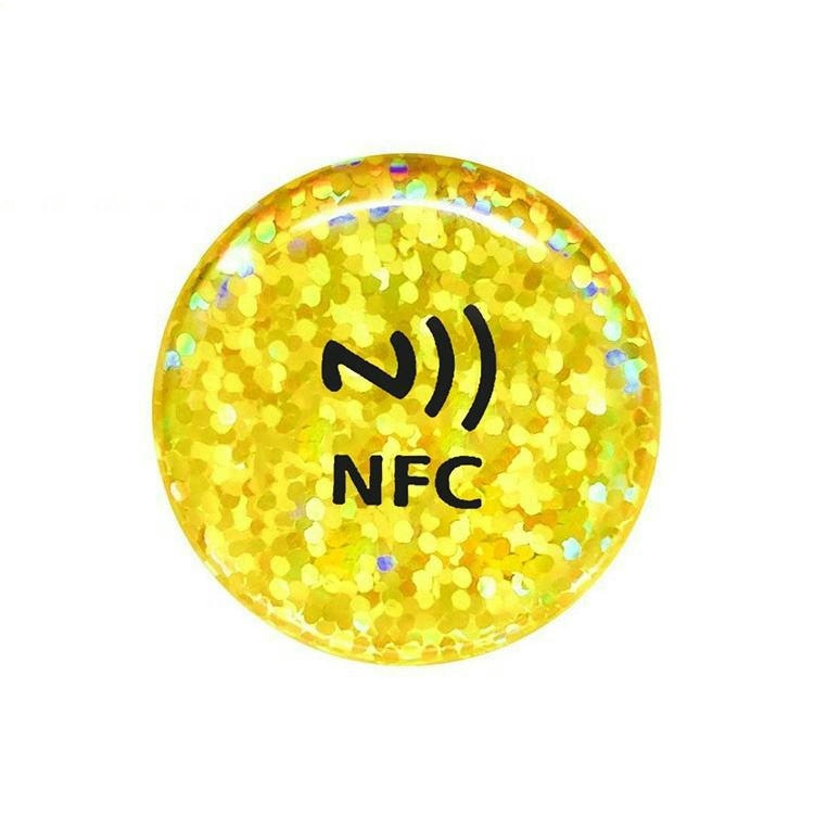 Et rundt NFC-epoxyklistermærke med guldglitter vist på hvid baggrund med dekorativ finish til loyalitets- og medlemsinteraktioner ved berøring.