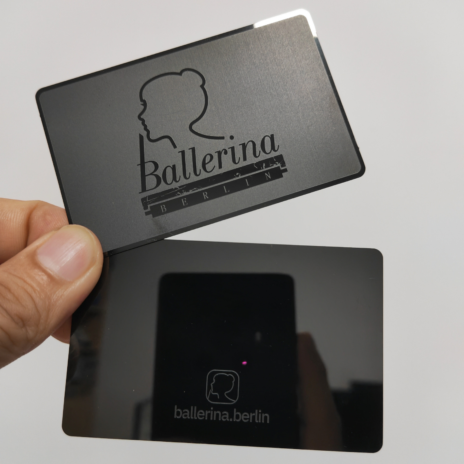 Sorte metalkort set forfra og bagfra med graveret logo og reflekterende bagside.
