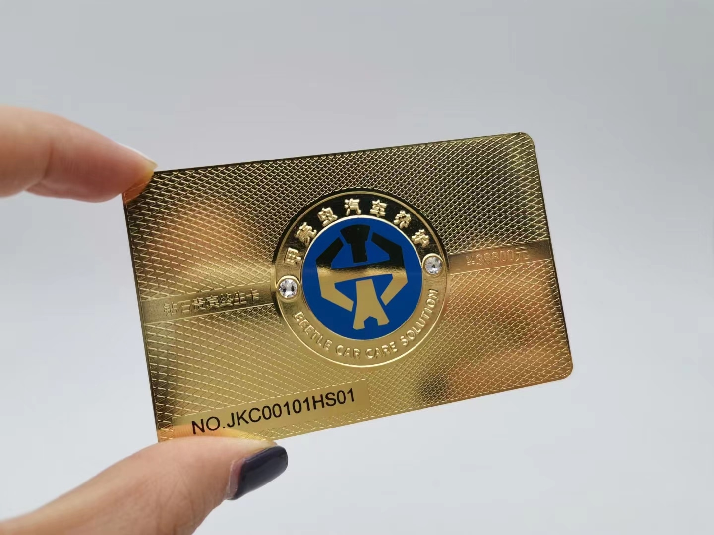 Tekstureret guldfarvet metalkort med emblem og eksklusiv overfladefinish.