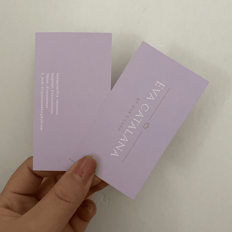 En hånd holder to lavendelfarvede, specialdesignede takkekort med brandlogo og kontaktoplysninger trykt i hvidt og guld.