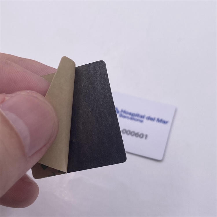 Nærbillede af en hånd, der løfter lineren fra et PVC RFID-tag til metal og viser klæbelaget klar til montering på metaludstyr.