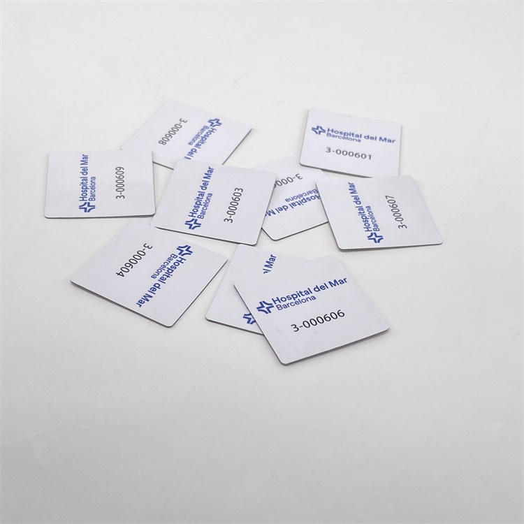 Flere firkantede PVC RFID-tags til metal ligger spredt på en hvid baggrund og viser trykt logo samt serienummer på de færdige tagoverflader.