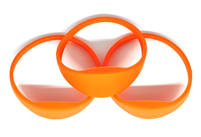 Frontfokuseret visning af orange G03B silikone RFID-armbånd arrangeret som sæt for at fremhæve det hævede område til RFID-tagging.