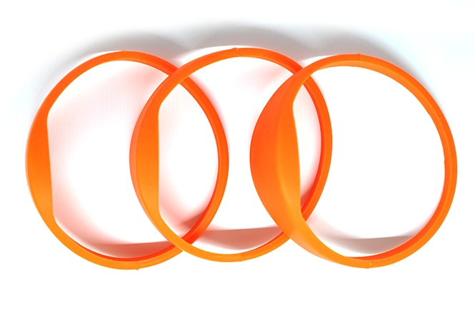 Tre orange G03B silikone RFID-armbånd lagt over hinanden set ovenfra for at vise den lukkede ringform og hovedets tykkelse.